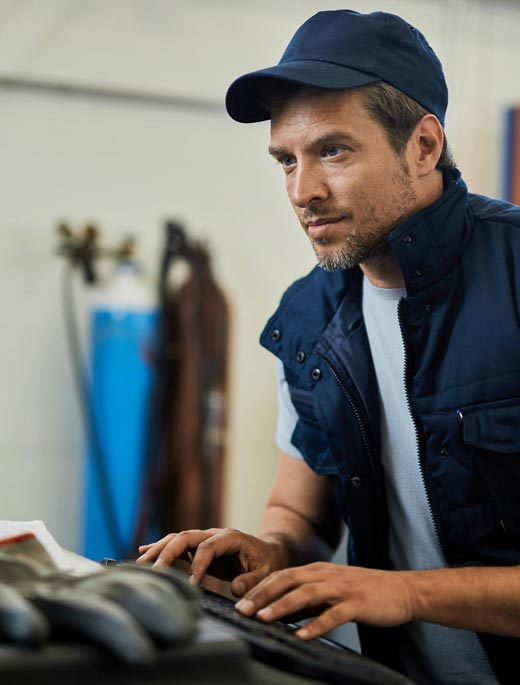 Trabajador con corra y chaleco azul haciendo una consulta en la computadora de un taller